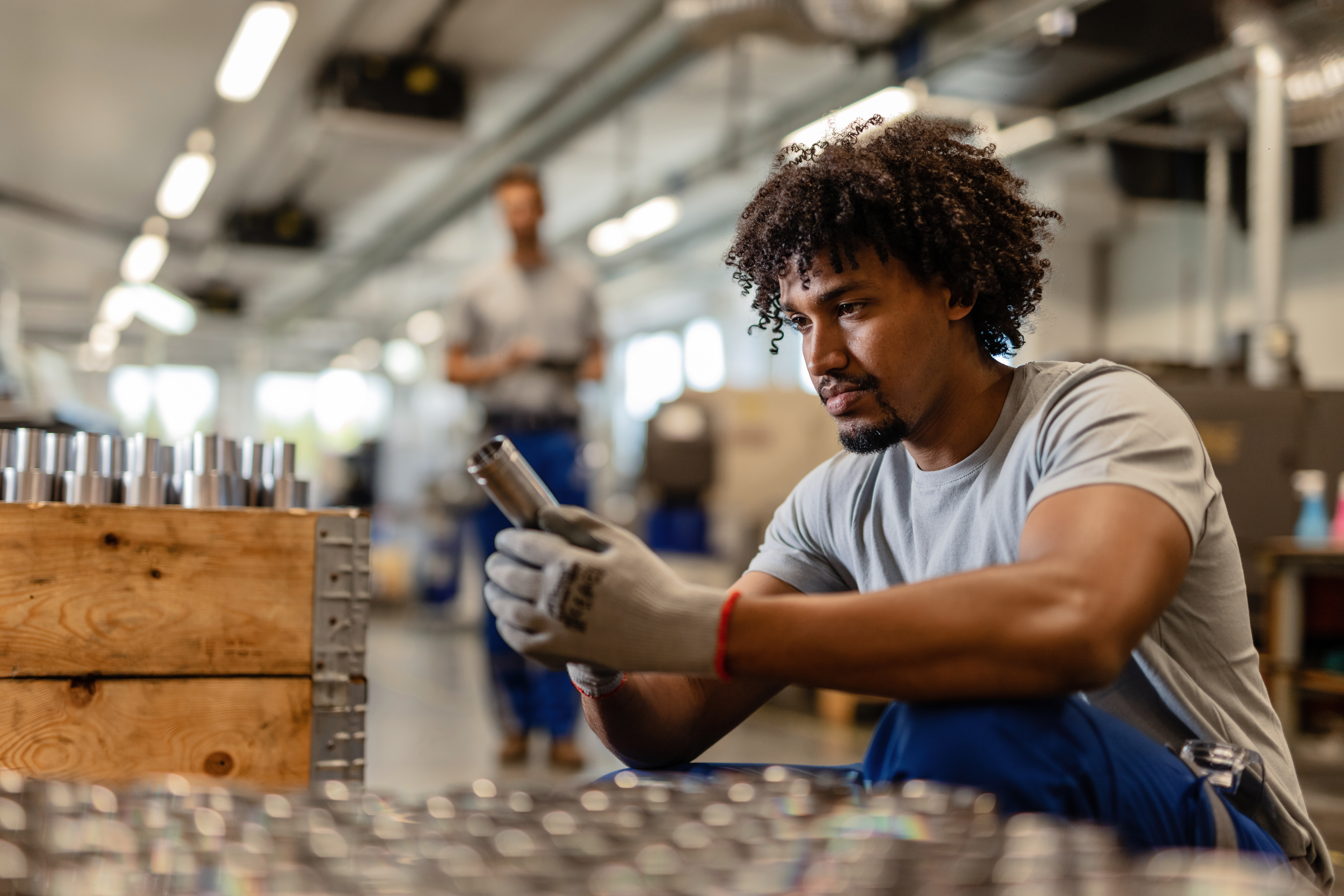 Young black worker examining stainless steel cylinder rod while working in distribution warehouse.