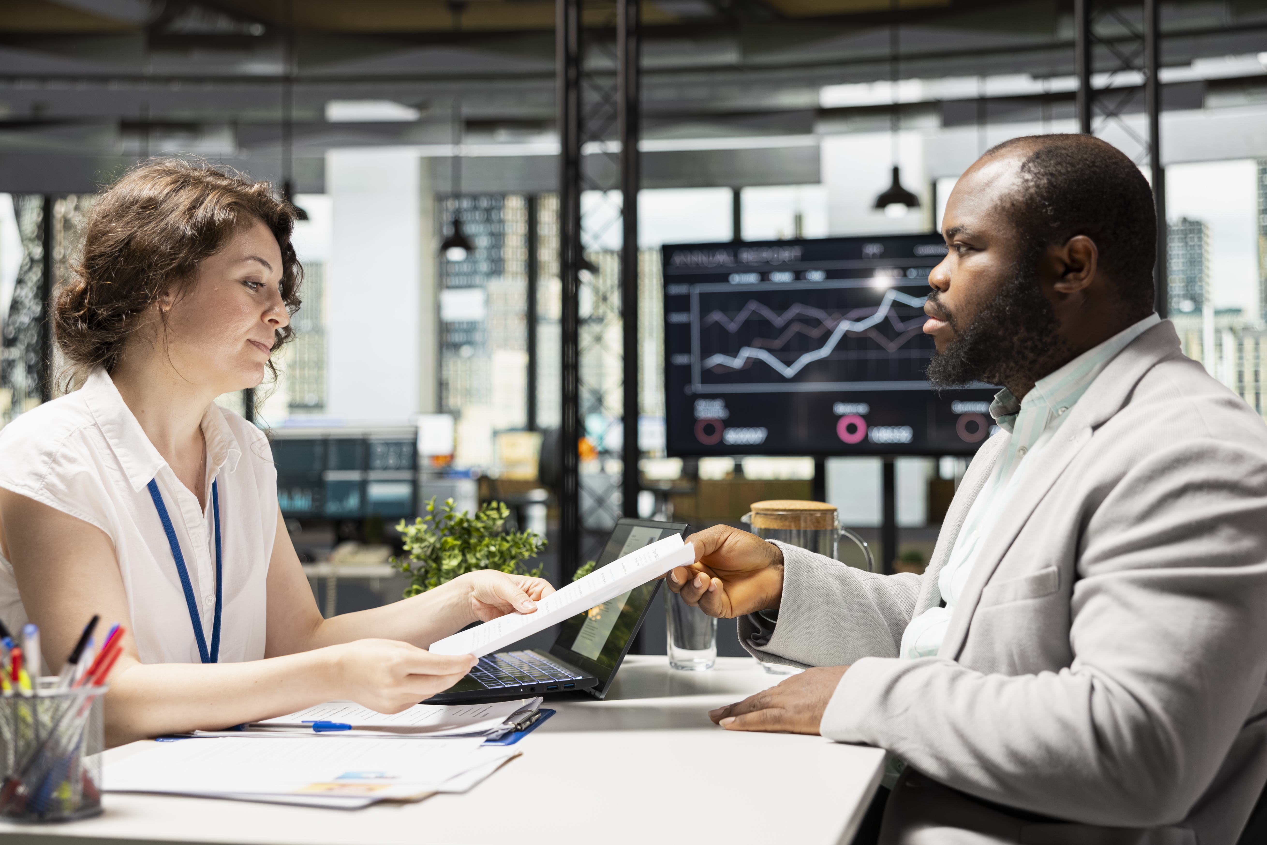 Black male candidate presenting CV information to HR assistant during a formal interview and evaluation, discussing job position requirements and qualifications needed for application.