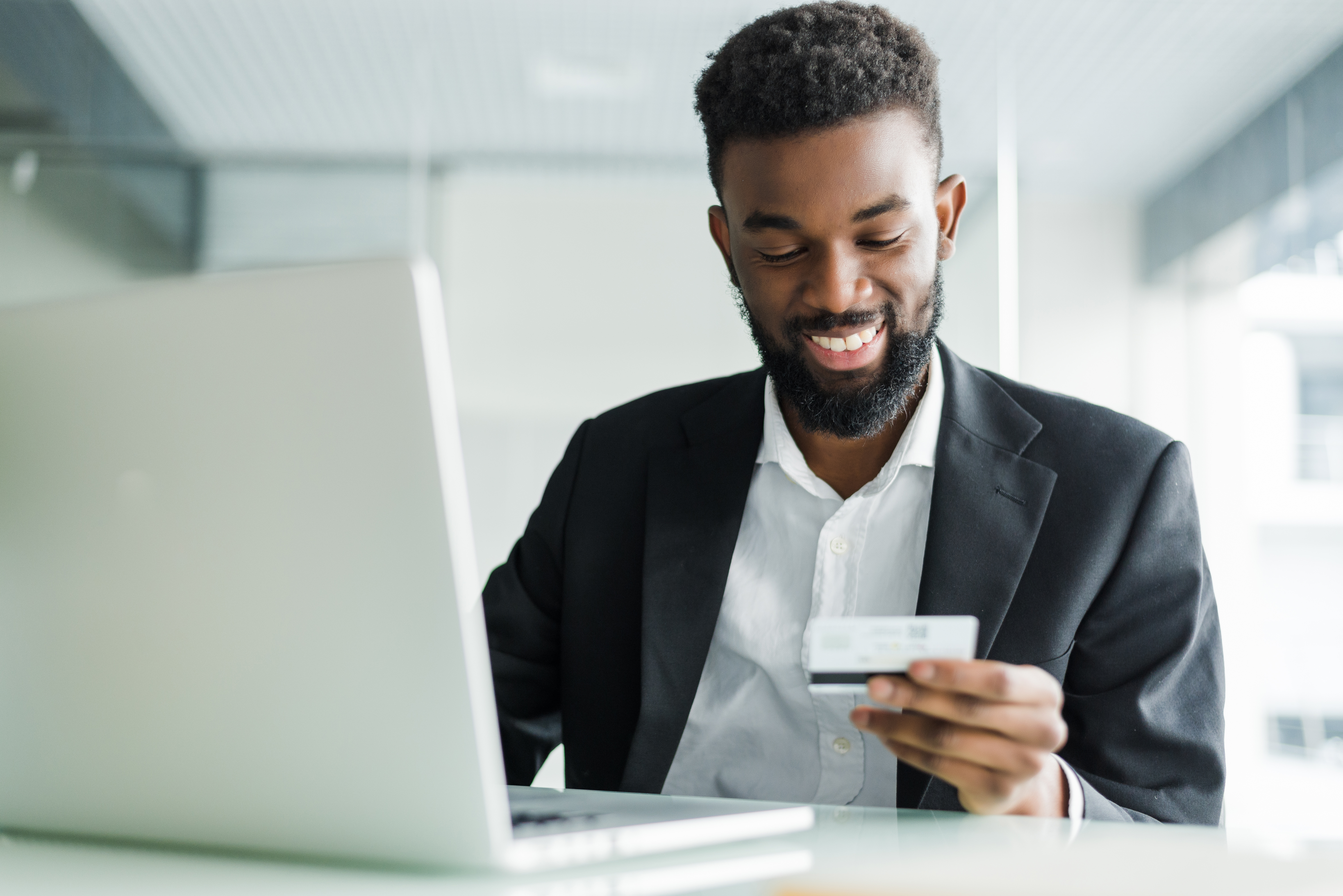 Successful African businessman sitting at a laptop and holding credit card in hand until businessman doing orders through the Internet