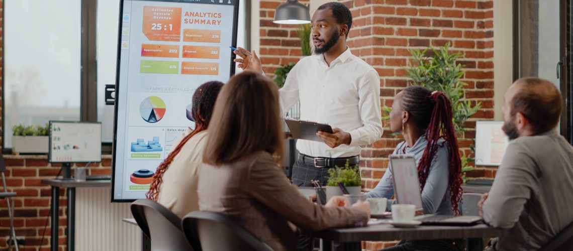Company employee presenting business strategy with charts on monitor, planning project. Workmates analyzing financial statistics on display, working together on company development.