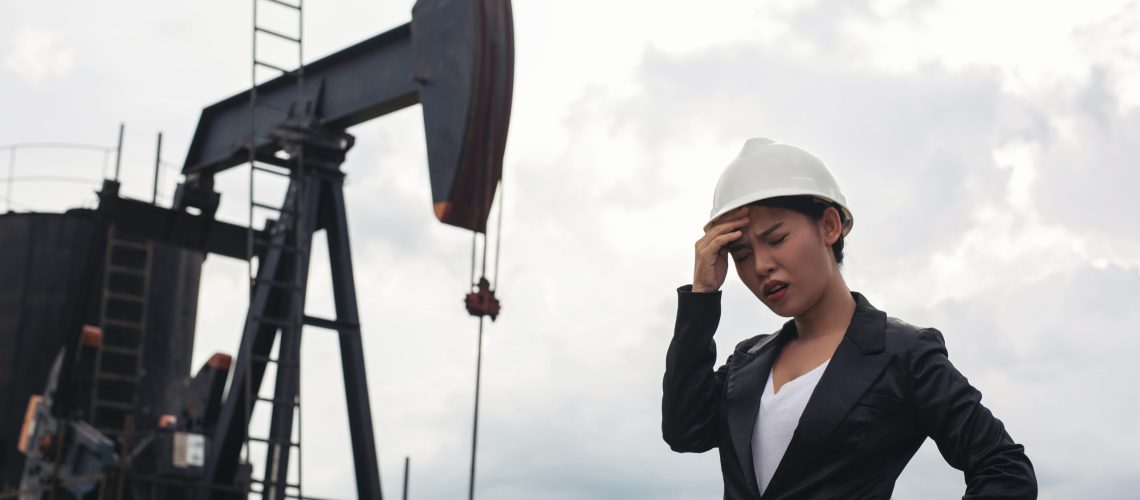 Female engineer standing with working oil pumps with a white sky background.
