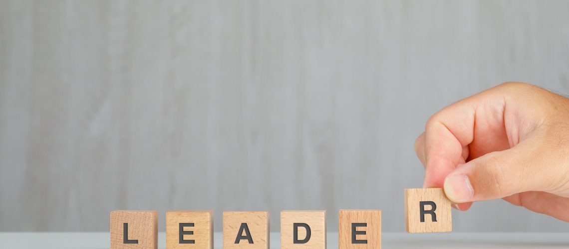 Leadership concept on grey and white background side view. hand picking up wooden cube.