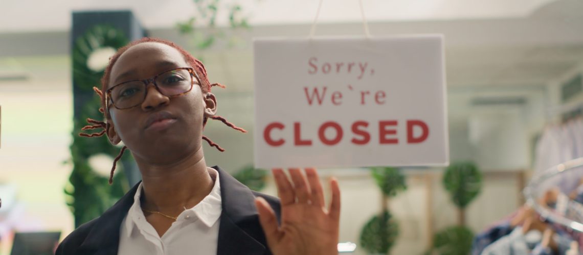 African american shop assistant closing fashion boutique business, ending her shift at night. Storekeeper turning opened sign on fast fashion clothing store into closed one after working hours