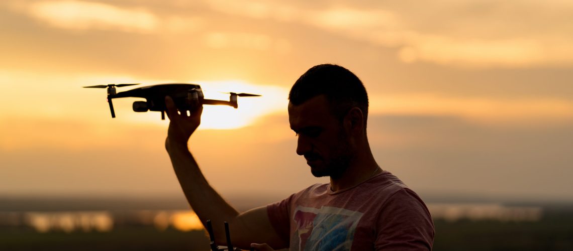 Silhouette of man piloting a drone at sunset with sunny sky in background