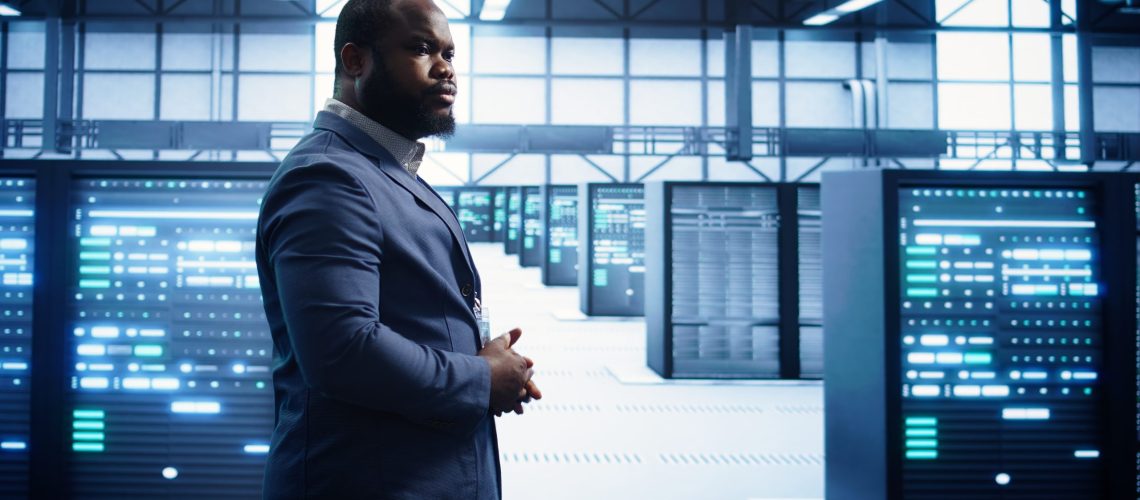 African american technician walking in data center, monitoring systems to identify errors. Man in server hub location doing diagnosis, looking for infrastructure bugs in need of repairing, camera B