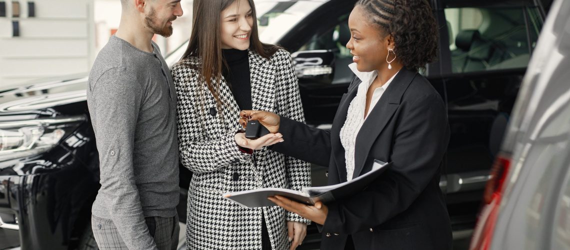 Young couple listening a sales agent about a car buying. Black female sales agent showing a documents and papers. Brunette caucasian man and woman is going to buy a car.